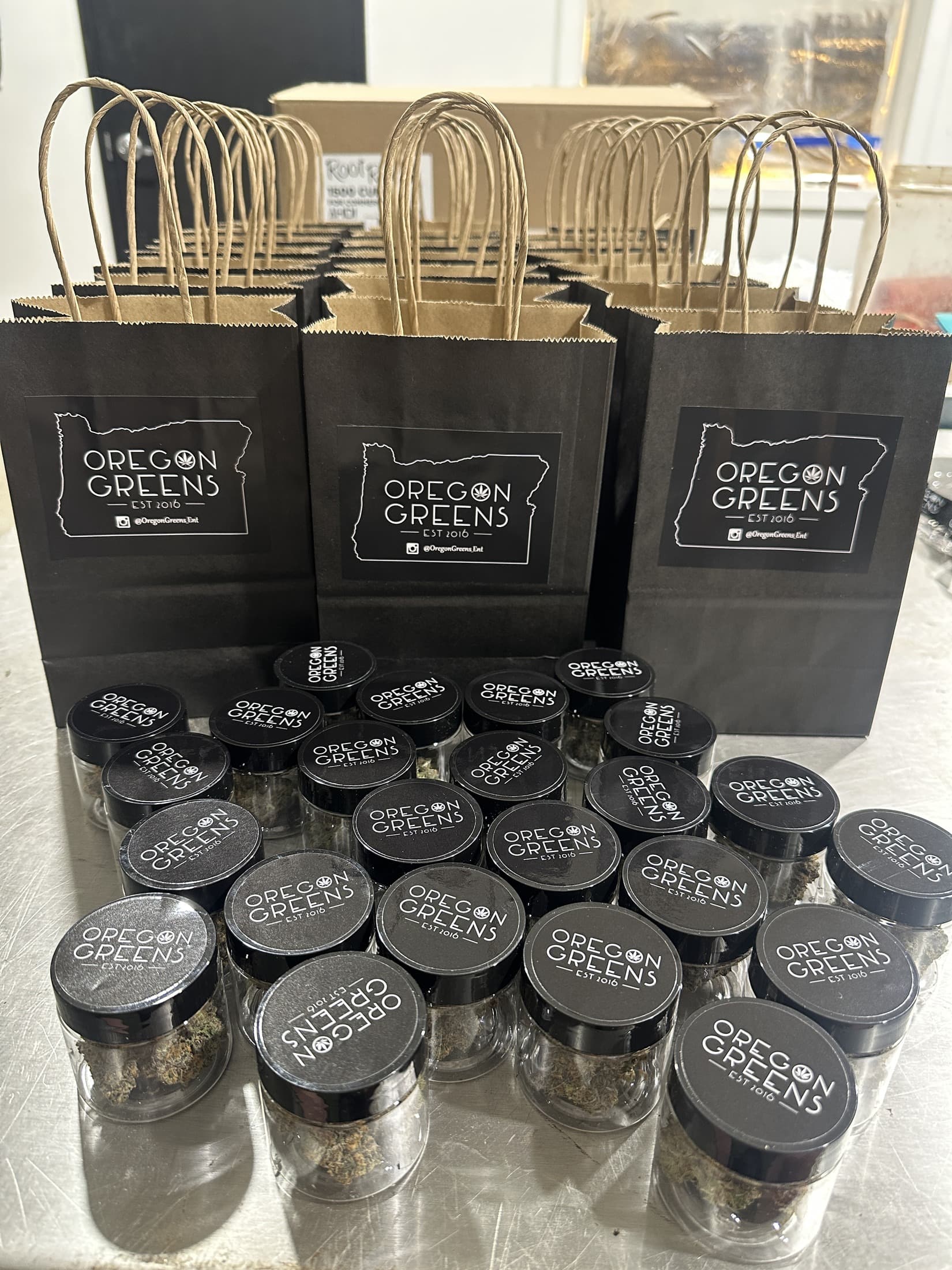 Oregon Greens branded jars, lids, and black paper bags arranged for retail packaging